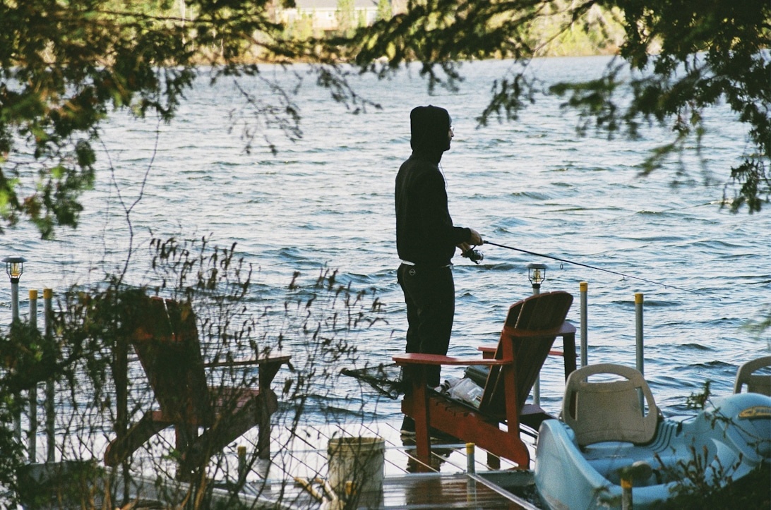 En fiskare i silhuett vid en sjö i solnedgången.